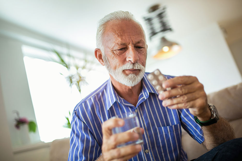 Senior man holding and examining antibiotic medication pills.