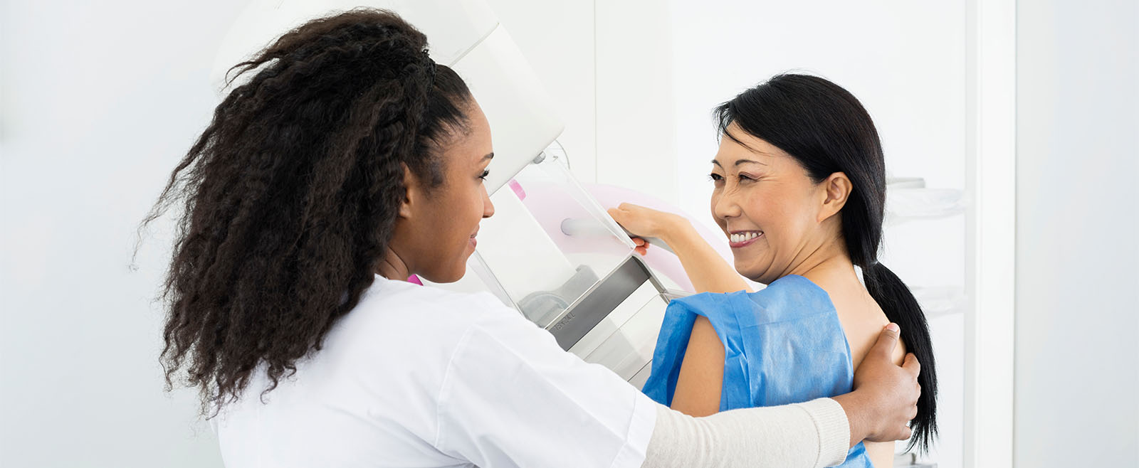 Happy woman looking at doctor while undergoing mammogram X-ray.